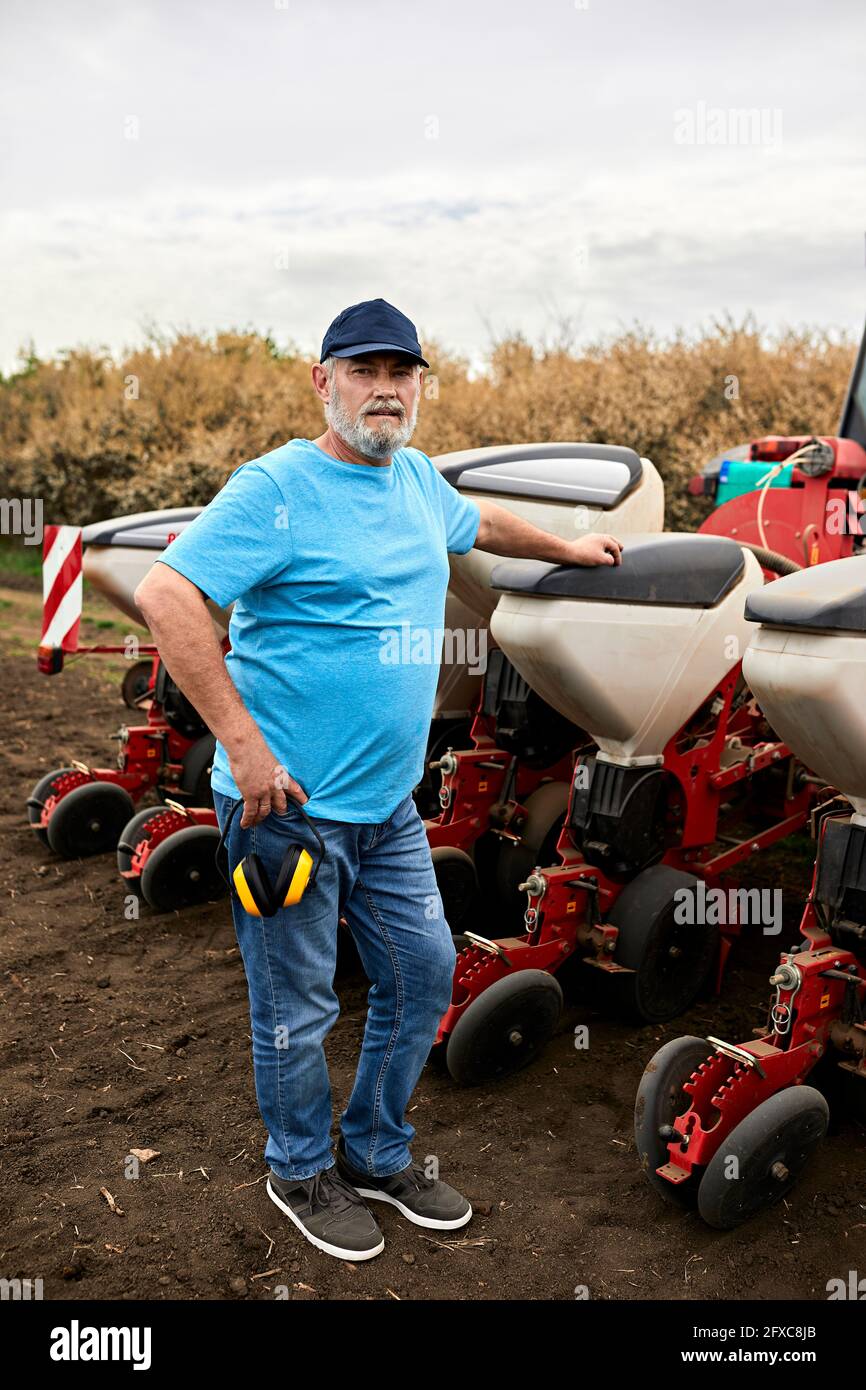 Agricoltore maschio maturo in piedi da trattore su campo agricolo Foto Stock