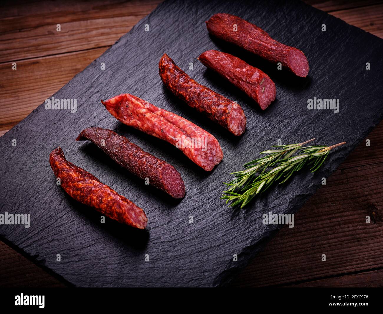 Salsiccia di Landjager con rosmarino su lastra di pietra ardesia nera Foto Stock