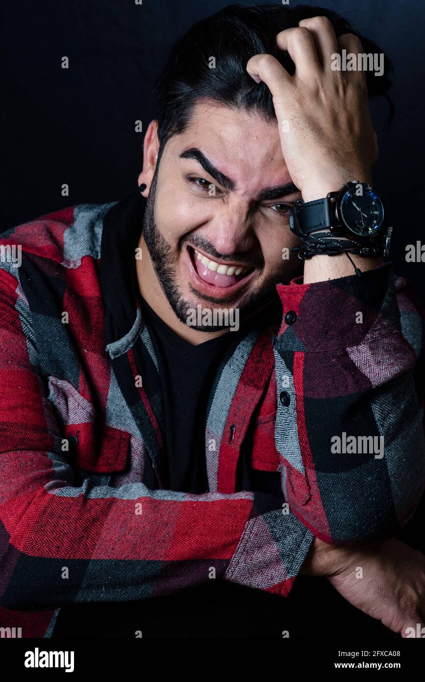 Uomo con mano in capelli che fa un viso su sfondo nero Foto Stock