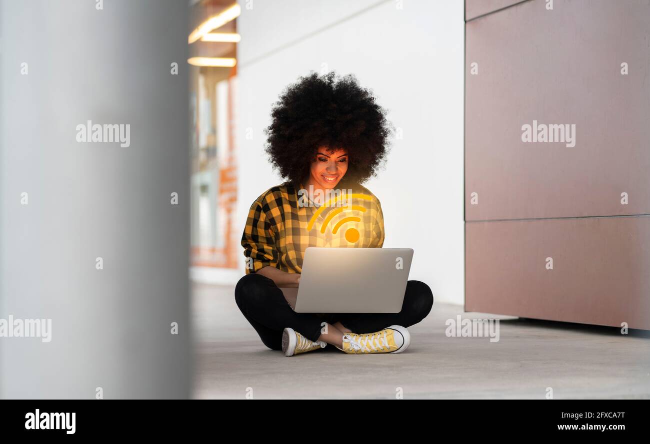Donna afro che usa un computer portatile con logo WIFI generato digitalmente Foto Stock