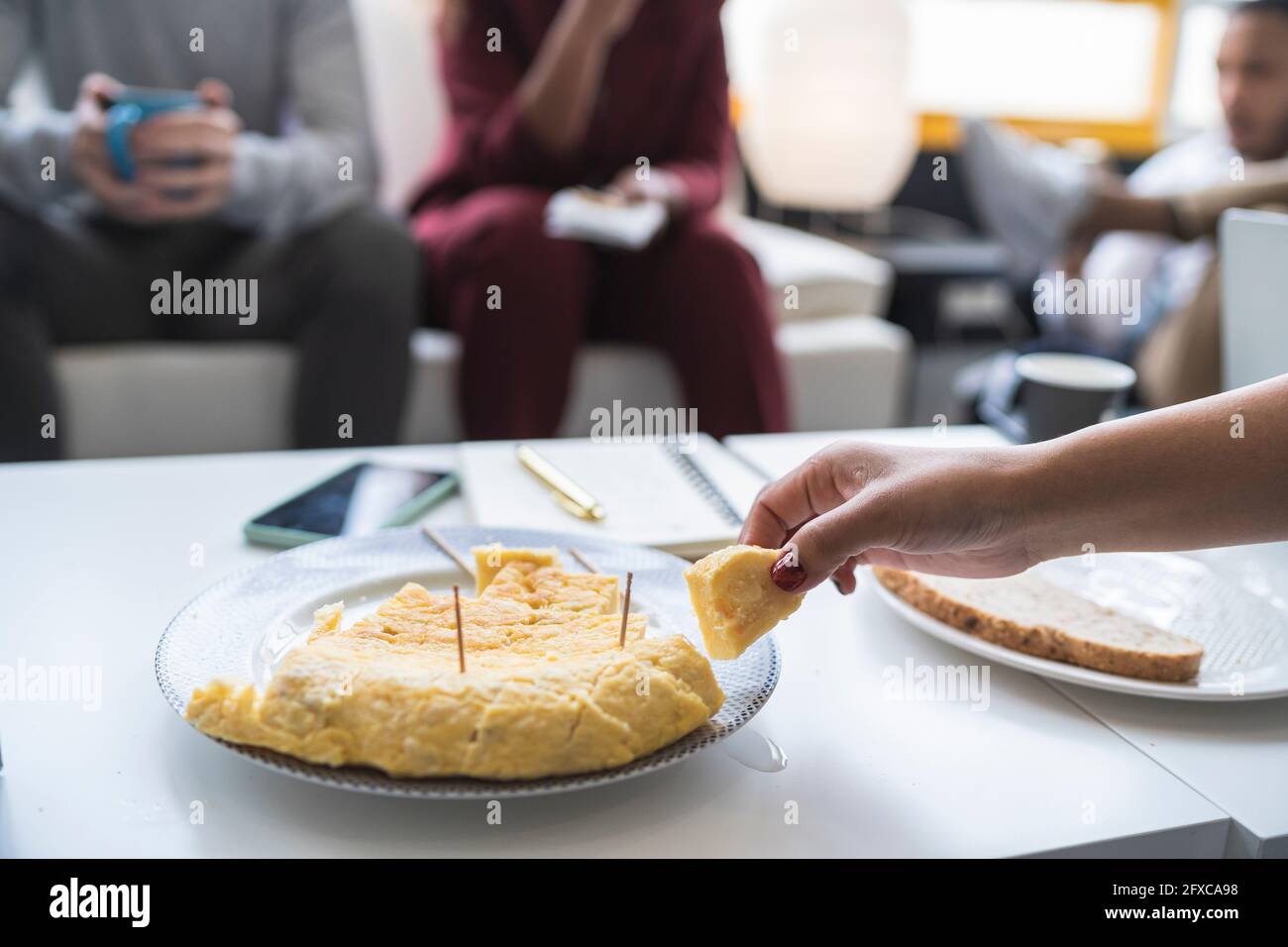 Donna d'affari che ha una frittata spagnola a tavola con colleghi in background Foto Stock