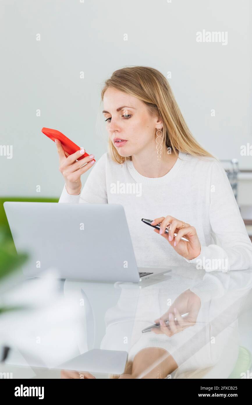 Donna imprenditore che invia la segreteria mentre si guarda il computer portatile in ufficio Foto Stock