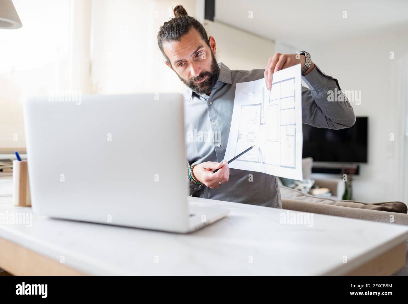Professionista del design maschile che mostra il piano di costruzione della videochiamata su un computer portatile a casa Foto Stock