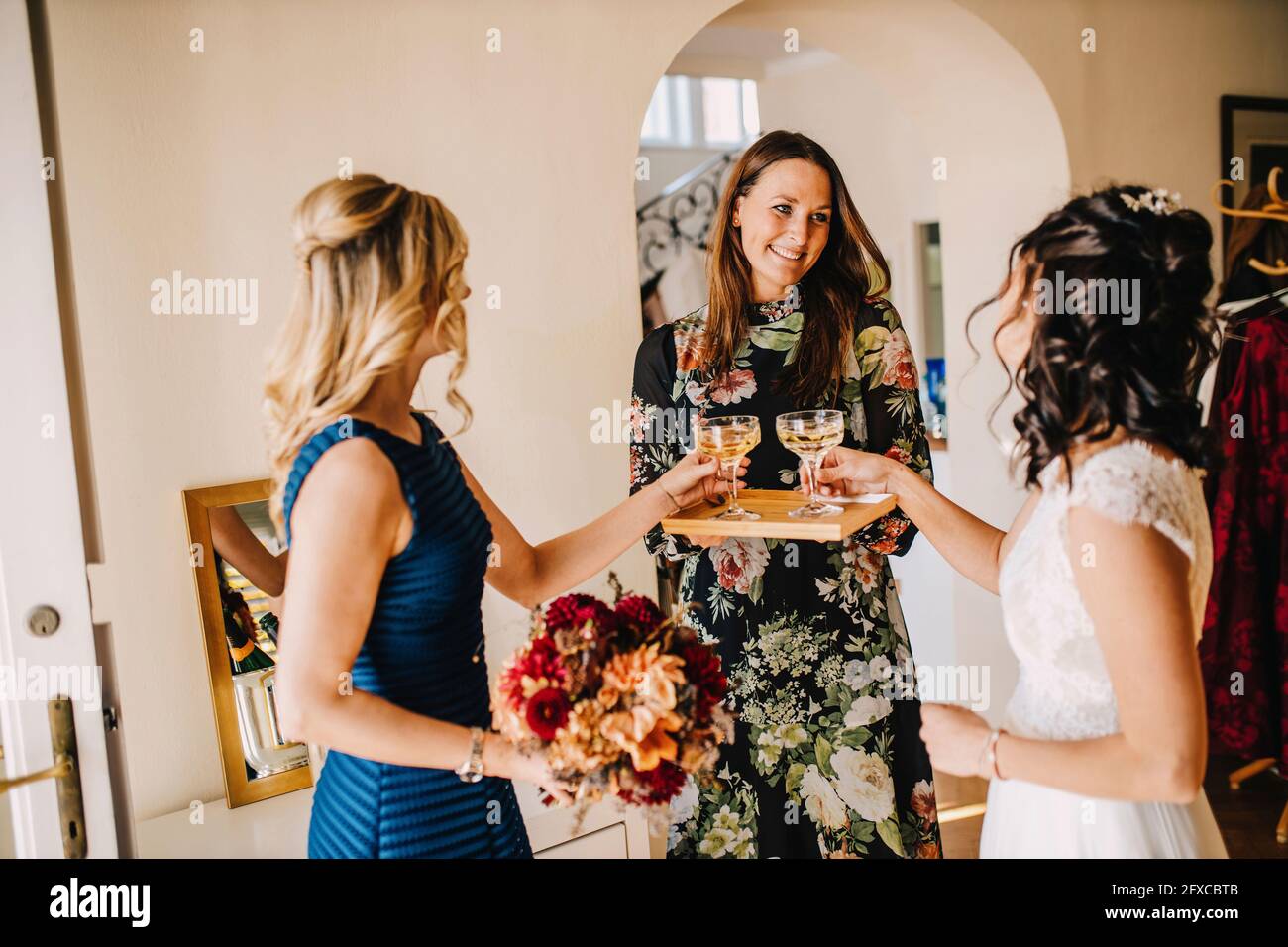 Donna sorridente che serve bevande alla sposa e alla cameriera in camera domestica Foto Stock
