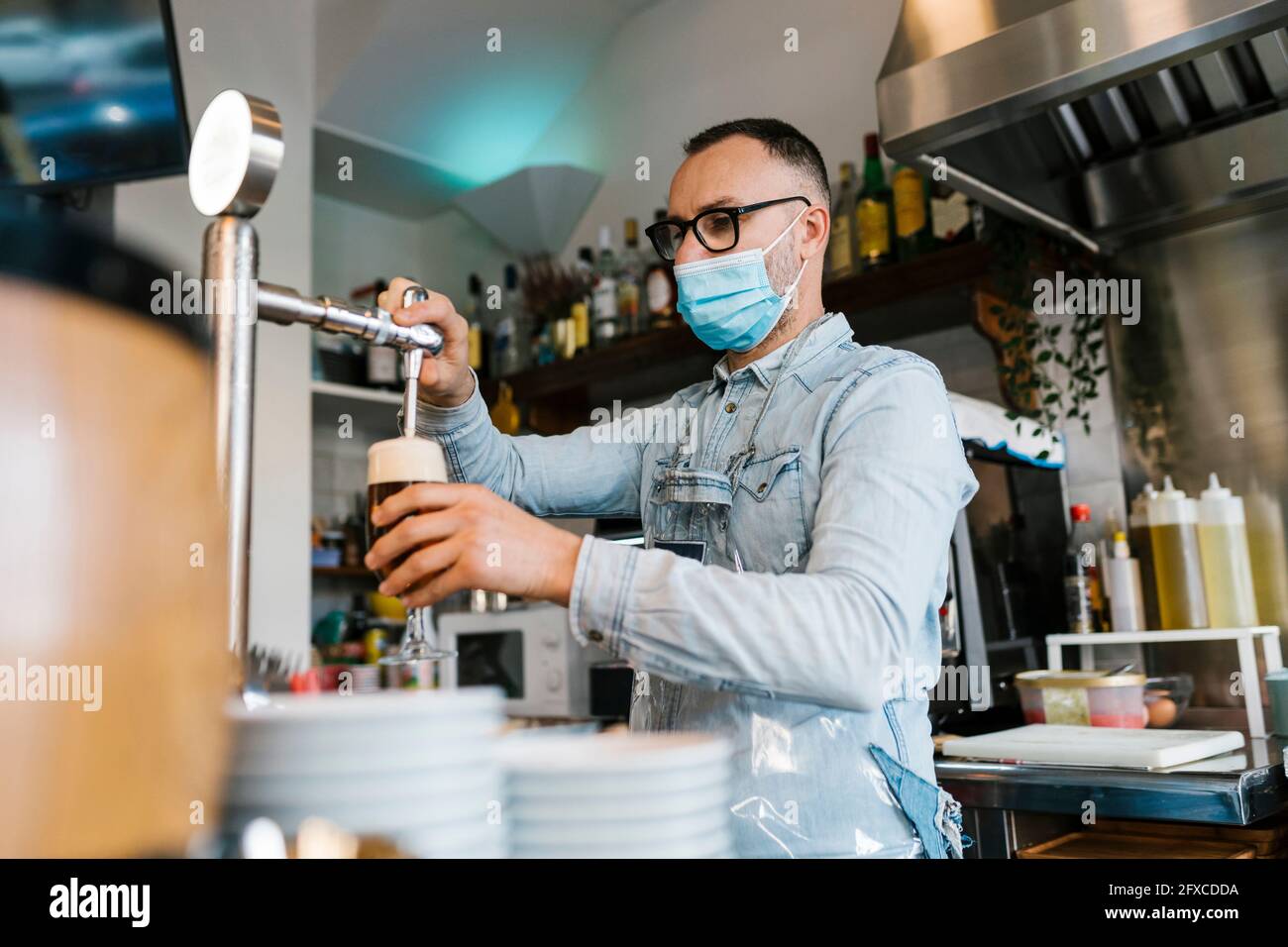 Cameriere che riempie la birra in un bicchiere in un bar durante la pandemia Foto Stock