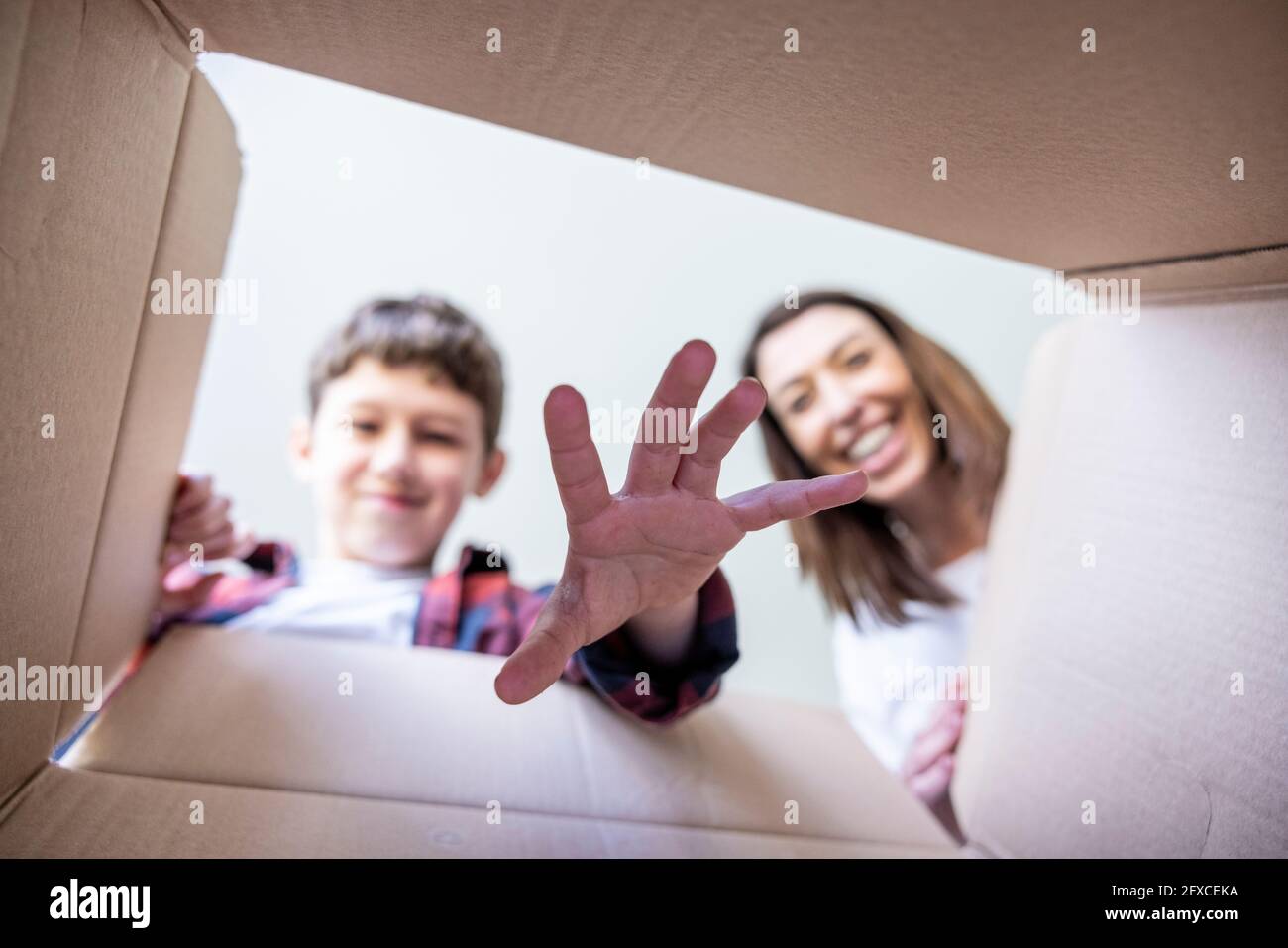 Figlio sorridente che mette la mano nella scatola di sorpresa dalla madre Foto Stock