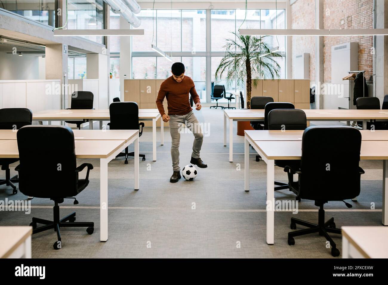 Giovane imprenditore che gioca con la palla di calcio in ufficio Foto Stock