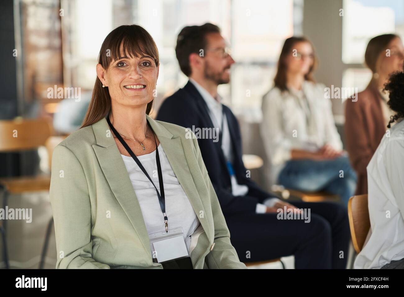 Donna d'affari sorridente seduta con i colleghi all'evento educativo in ufficio Foto Stock