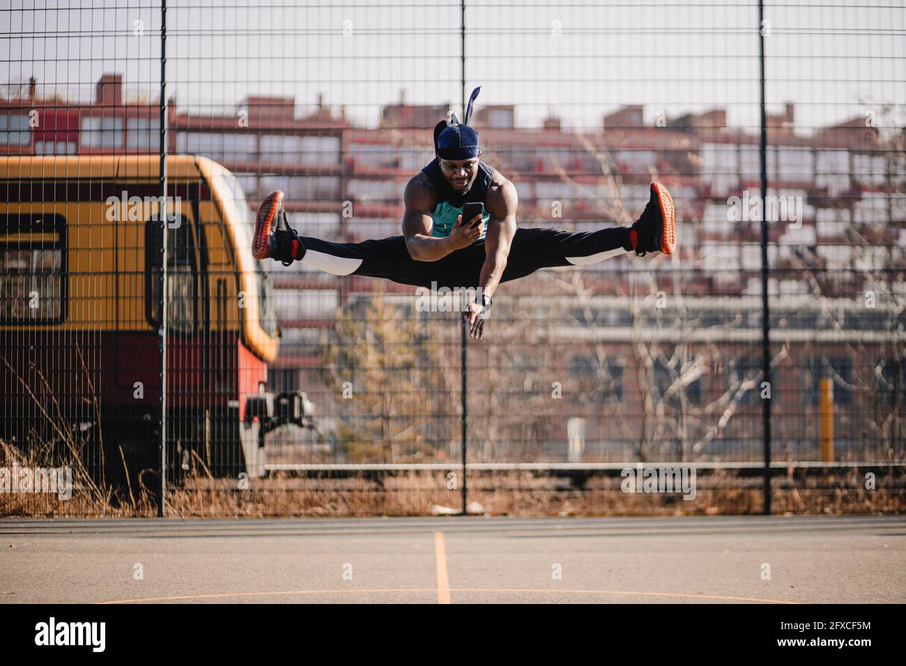 Uomo africano che usa il telefono cellulare mentre salta sul campo sportivo Foto Stock