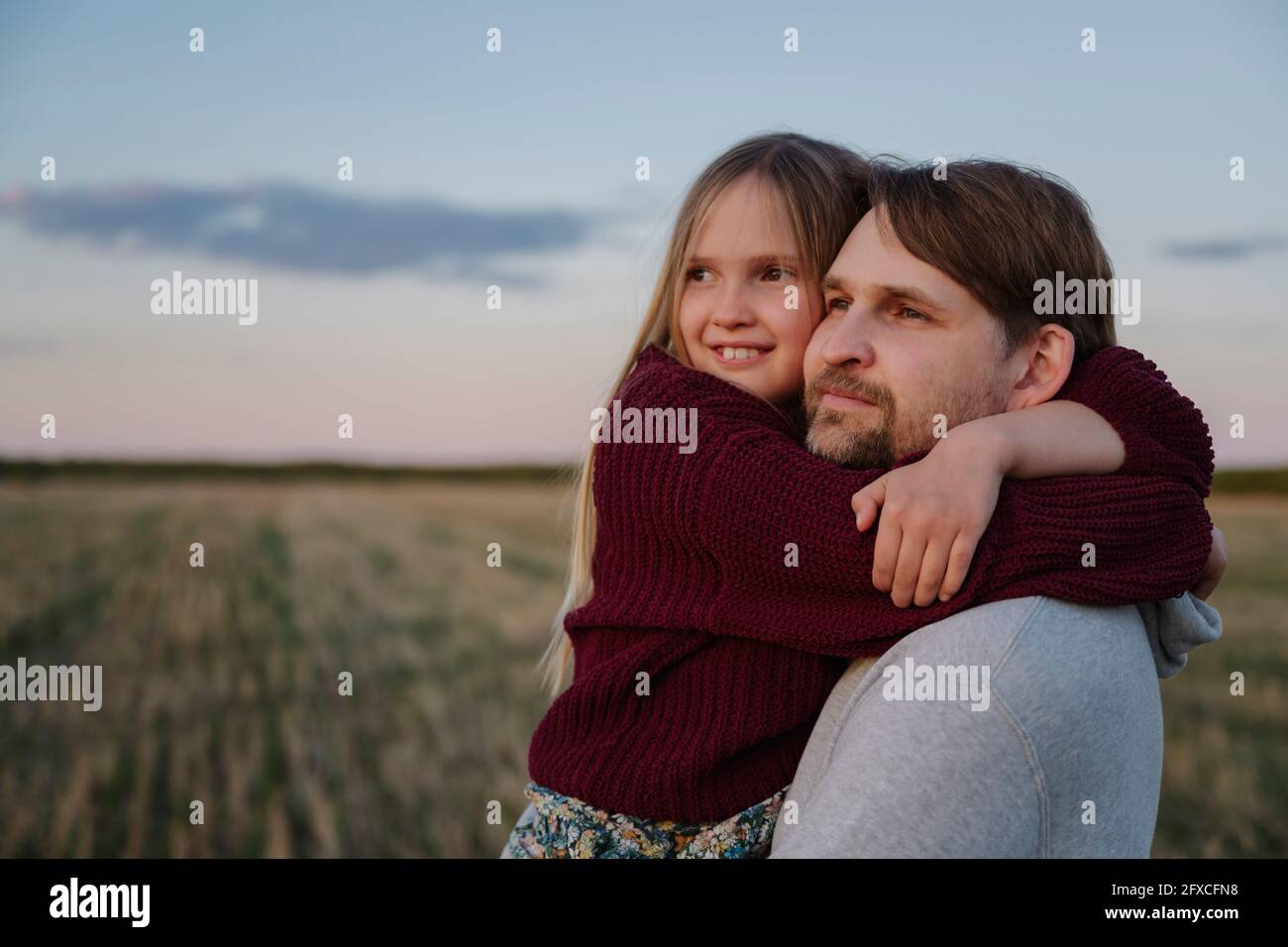 Figlia abbracciando il padre mentre guarda il tramonto Foto Stock