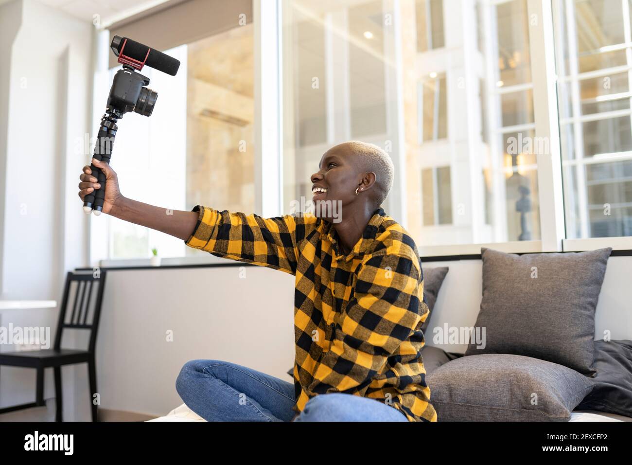Donna sorridente che tiene la videocamera mentre si siede a letto a casa Foto Stock
