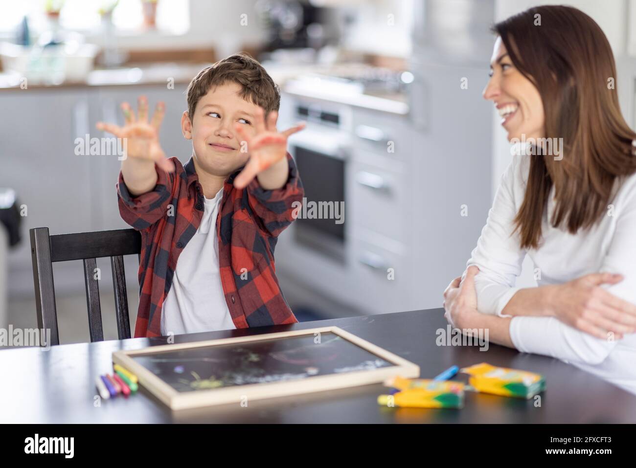 Ragazzo che mostra le mani sporche mentre si guarda con uno sguardo laterale alla madre in cucina Foto Stock
