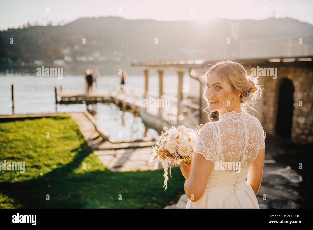 Bella sposa con bouquet che si affaccia sulla spalla in giornata di sole Foto Stock