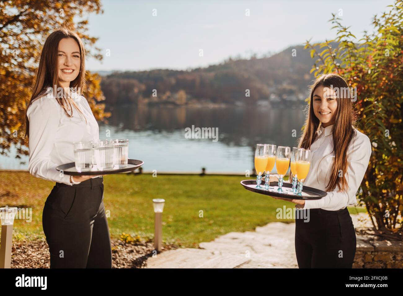 Cameriere in piedi con vassoio in giardino vicino al lago durante il giorno di sole Foto Stock