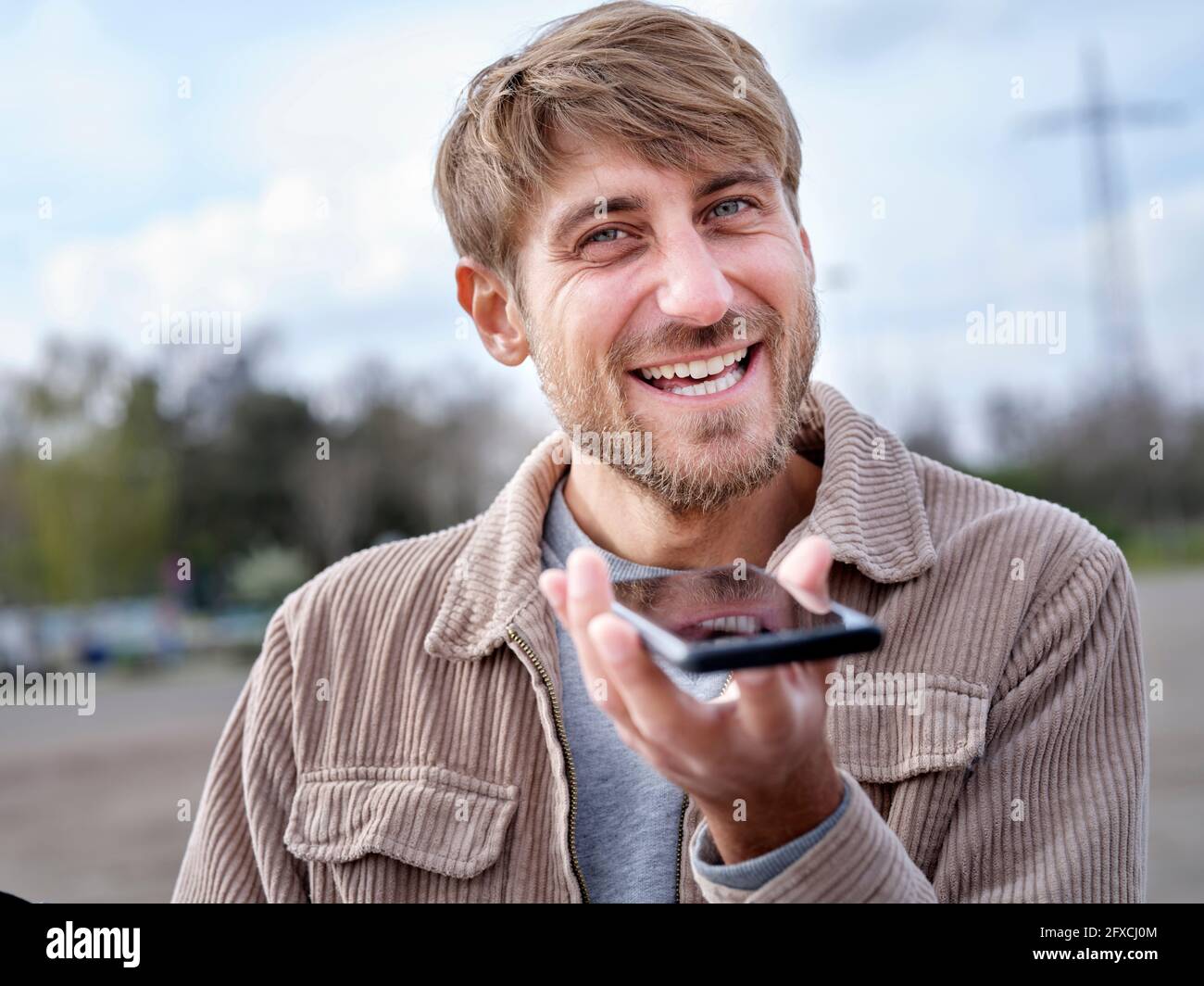 Uomo sorridente che invia messaggi vocali tramite telefono cellulare Foto Stock