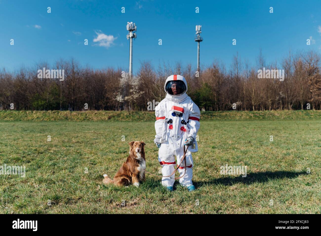 Astronauta femminile in tuta spaziale in piedi con cane su erba Foto Stock