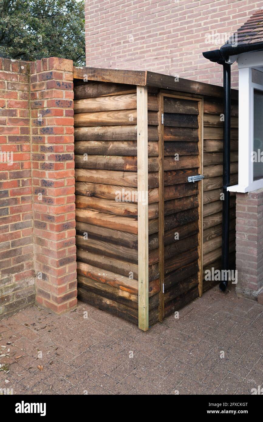 Capannone di legno di recente costruzione come una capannone di attrezzi o area di deposito di ceppo costruito contro una parete circostante di mattone. Foto Stock