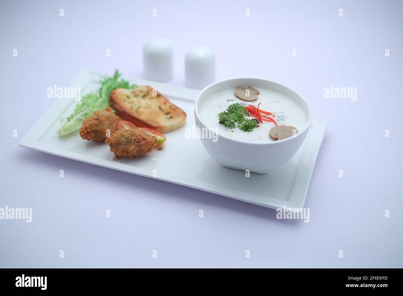 Crema di funghi zuppa disposta in una ciotola bianca con pane tostato e insalata di verdure fresche come contorno sistemato su una tavola da portata bianca Foto Stock