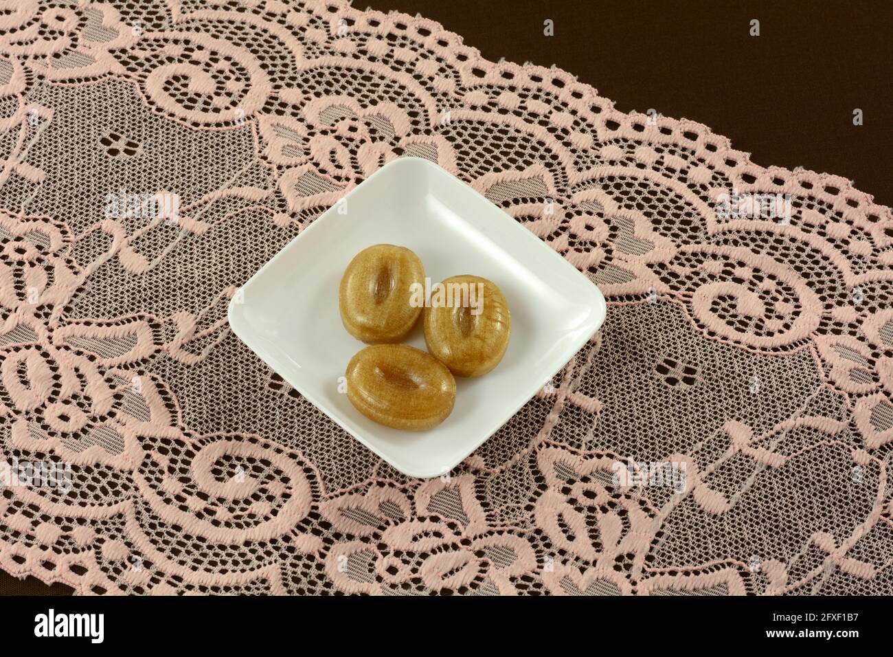 Thai tamarind caramelle dure pezzi su piccola piastra caramella su pizzo rosa su tovaglia marrone Foto Stock