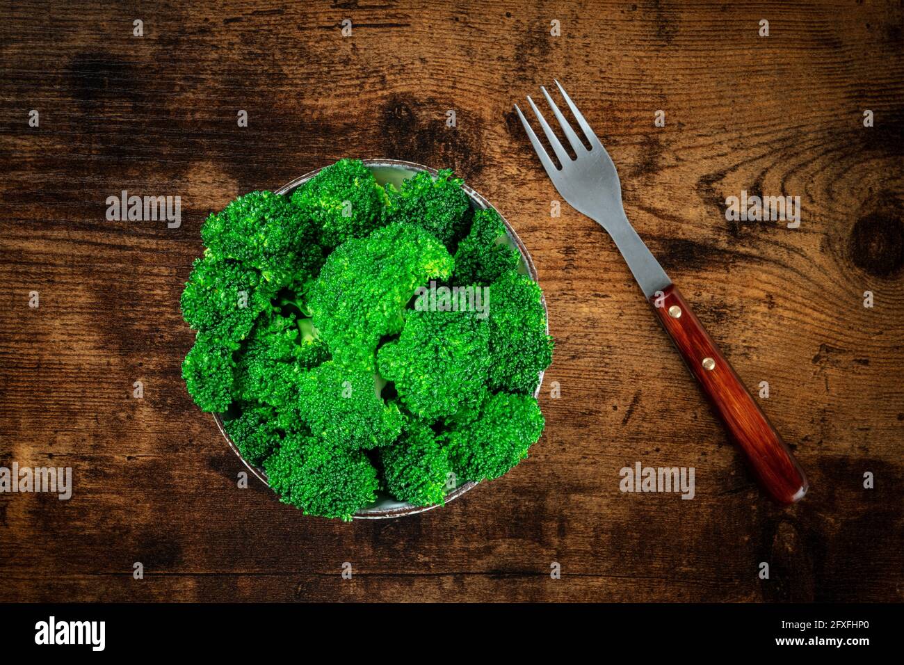 Broccoli in una ciotola con una forchetta, colpo d'alto su uno sfondo di legno rustico scuro. Pasto vegano sano Foto Stock