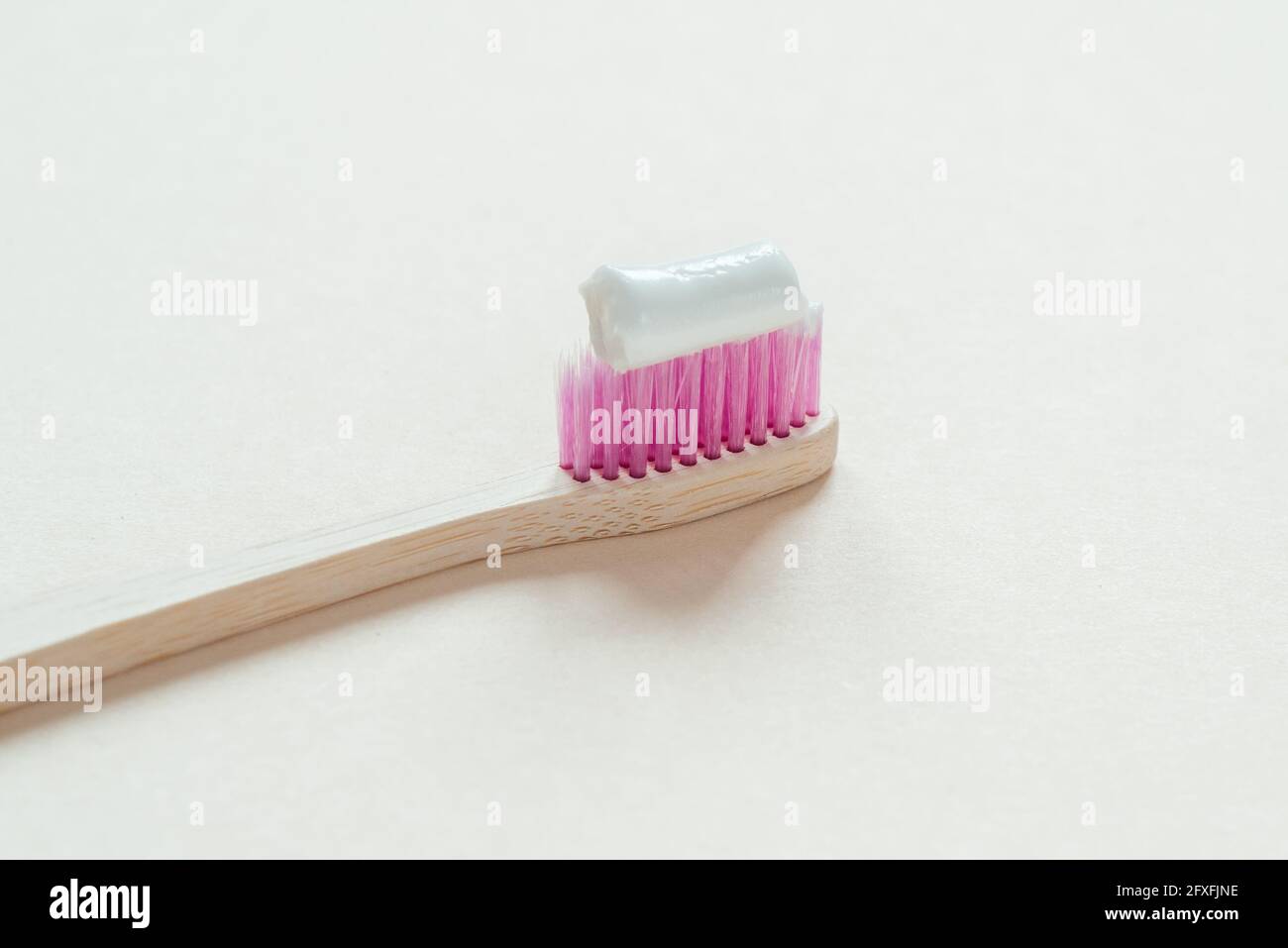 Spazzolino in bambù rosa con pasta dentaria su di esso primo piano, cura dentale con concetto zero rifiuti, stile di vita sostenibile Foto Stock