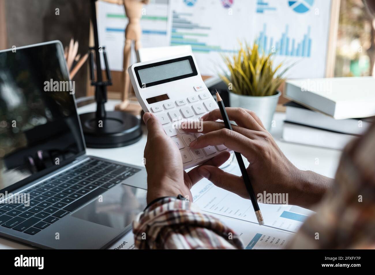 Il contabile sta usando una calcolatrice per calcolare i dati finanziari dell'azienda dai fogli di guadagno, un uomo d'affari seduto nel suo ufficio dove l'azienda Foto Stock