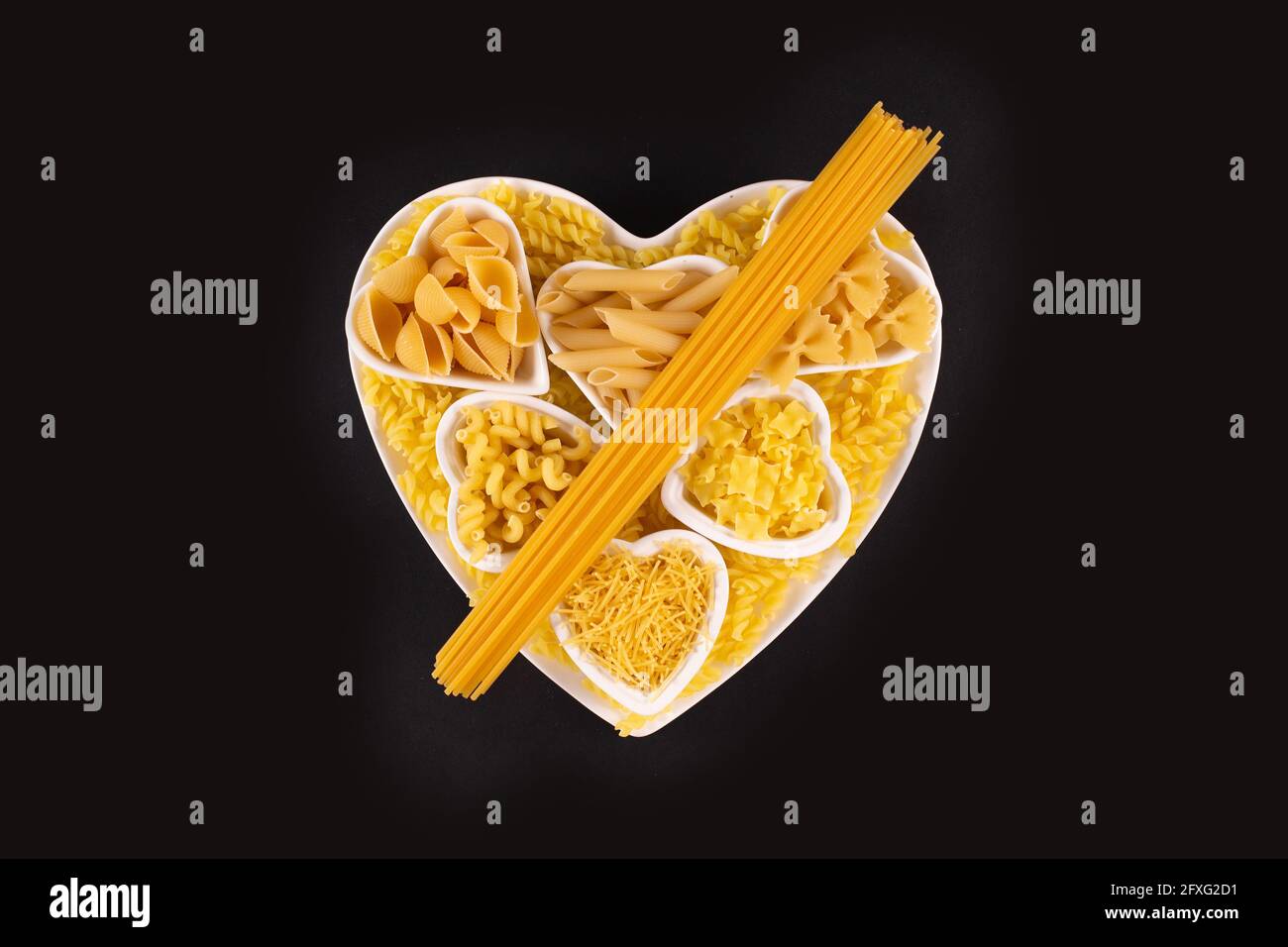 Selezione di piatti di pasta in porcellana a forma di cuore su sfondo nero. Tagliatelle di pasta essiccate e non cotte. Concetto di pasta d'amore Foto Stock
