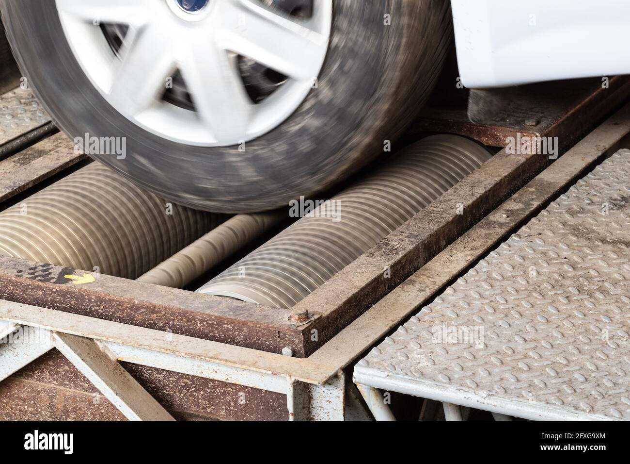 Ruota del veicolo rotante sul tester del freno a rulli durante l'ispezione MOT corsia in officina Foto Stock