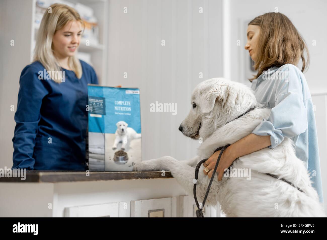 Donna proprietaria con grande cane bianco alla reception in clinica veterinaria scegliendo cibo secco per l'animale domestico. Il cane salì le zampe sul tavolo. Cura e trattamento degli animali domestici Foto Stock
