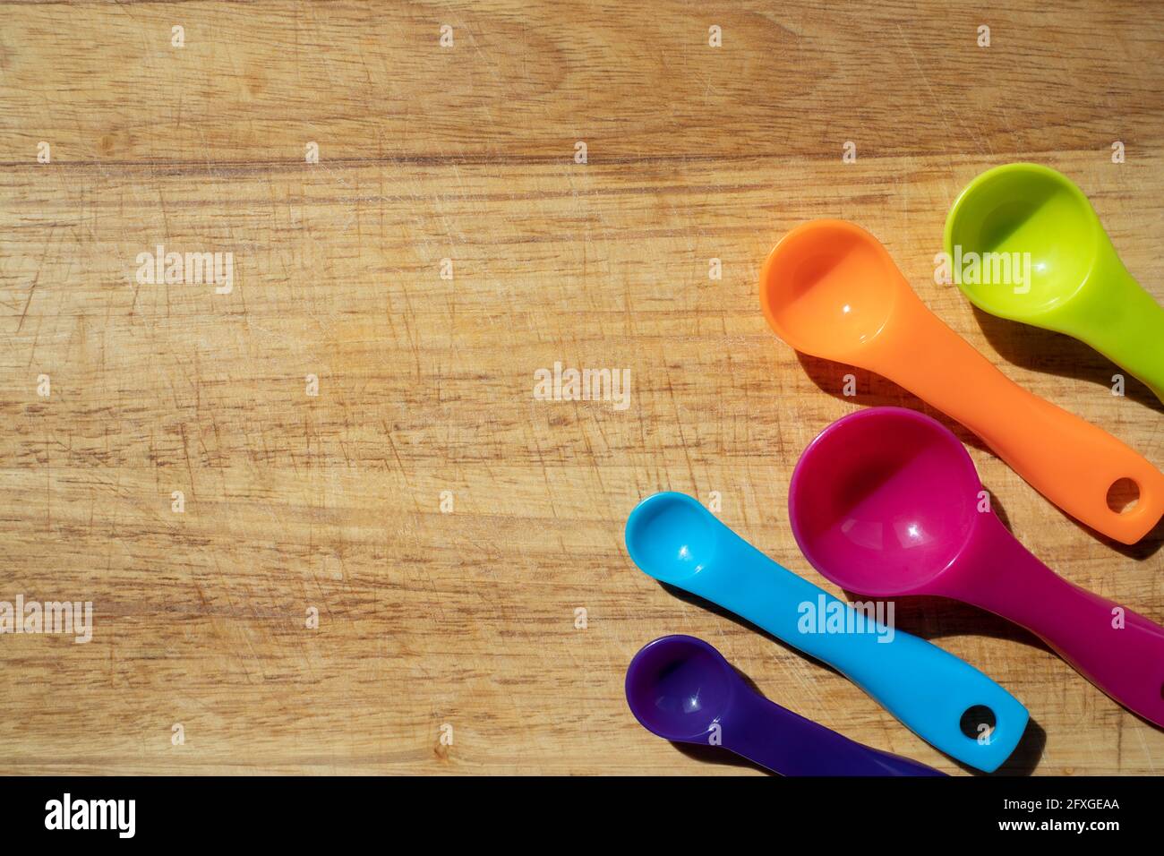 Usato tagliere da cucina in legno con colorati cucchiai di misurazione in angolo. Vista dall'alto del banner Foto Stock