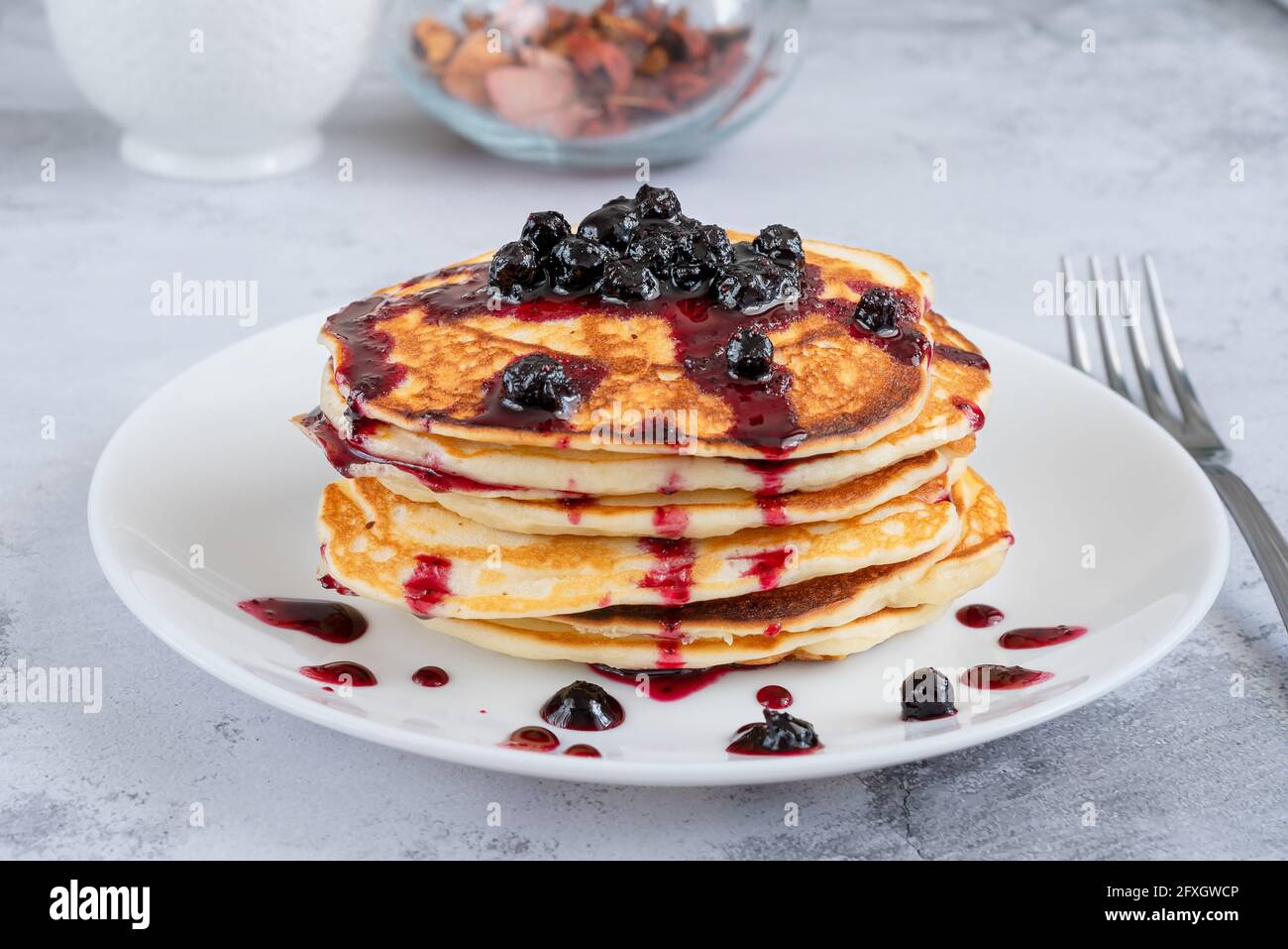 Piccole frittelle con marmellata di mirtilli per colazione sul tavolo da cucina. Cibo dolce e buon umore Foto Stock