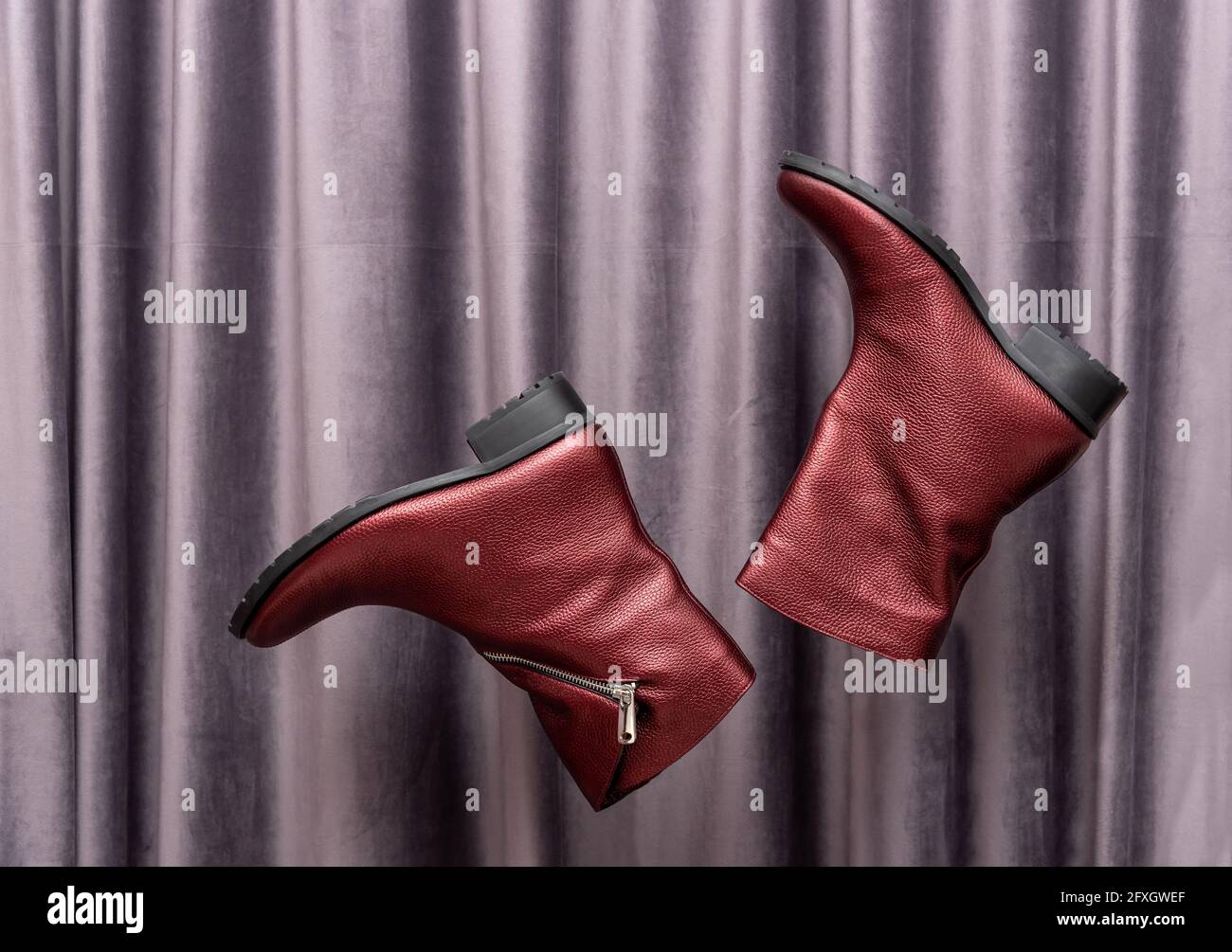 Gli eleganti stivali da donna in pelle rossa volano contro la tenda viola Foto Stock