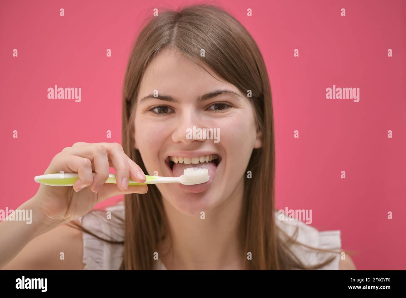Giovane Donna pulizia lingua utilizzando spazzolino in studio Foto Stock