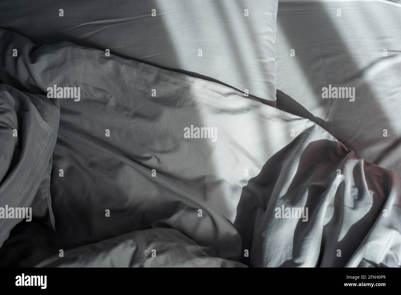 Letto comodo con cuscini e coperta in camera ombreggiata Foto Stock