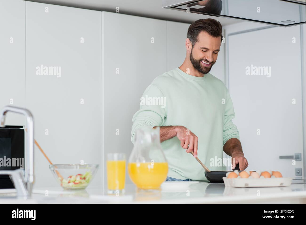 uomo sorridente che prepara la colazione sulla penna per friggere in cucina Foto Stock