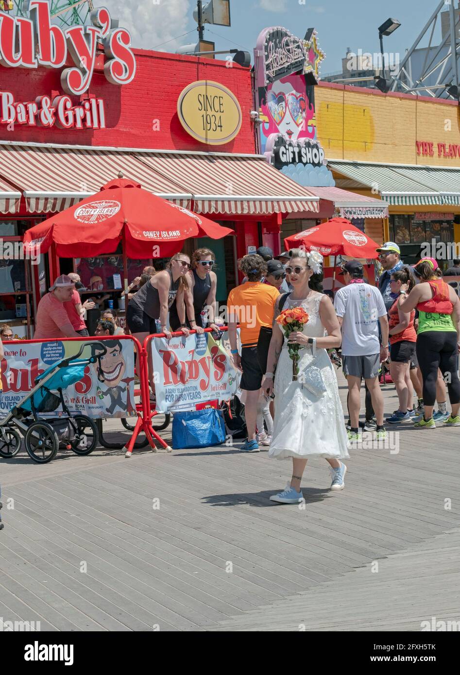 Poco dopo il suo matrimonio sulla spiaggia una nuova sposa cammina sul lungomare di Coney Island mentre tiene un mazzo di fiori. Foto Stock