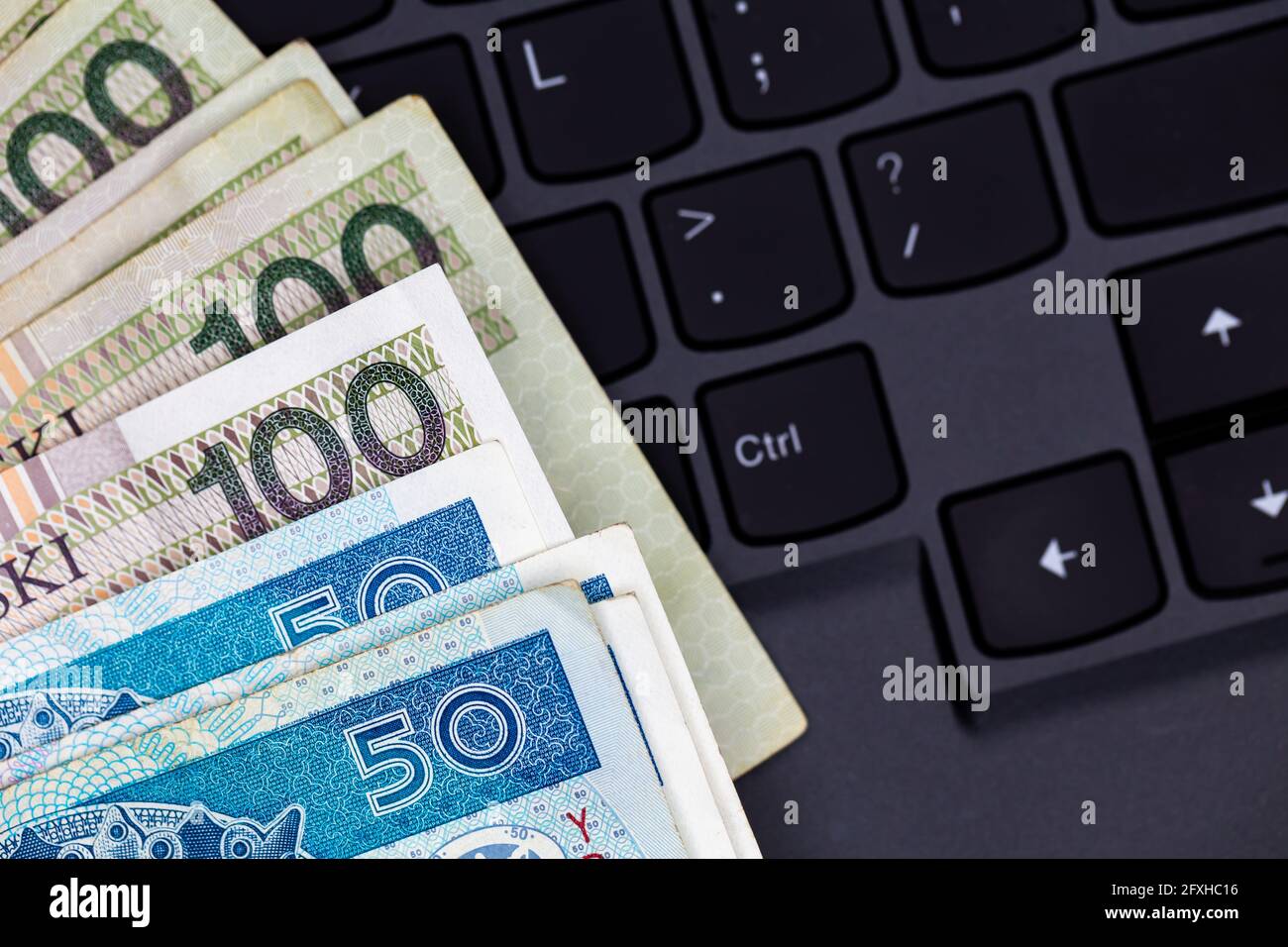 Un set di banconote da 50 e 100 PLN polacche disposte su una tastiera nera per laptop. Foto scattata in condizioni di luce artificiale e soffusa Foto Stock