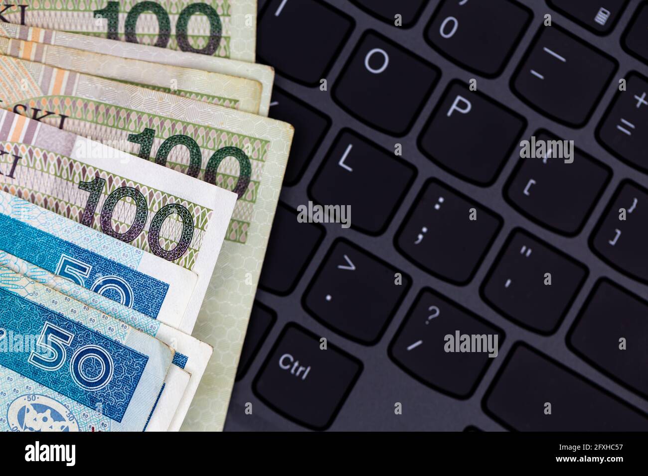 Un set di banconote da 50 e 100 PLN polacche disposte su una tastiera nera per laptop. Foto scattata in condizioni di luce artificiale e soffusa Foto Stock