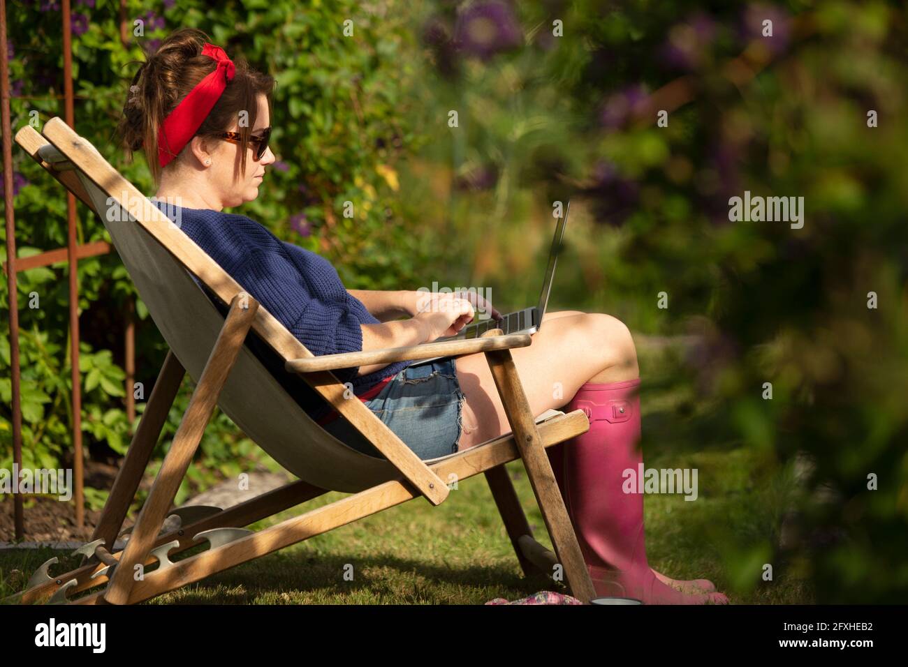 Donna che lavora su un computer portatile in sedia da prato nel soleggiato giardino estivo Foto Stock