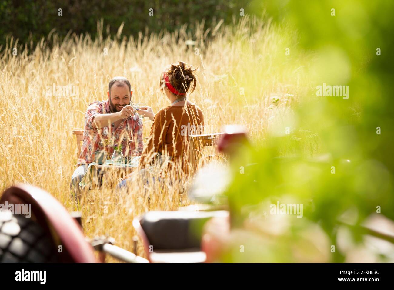 Accoppia i bicchieri d'acqua per tostare in un'erba alta e soleggiata dietro il trattore Foto Stock