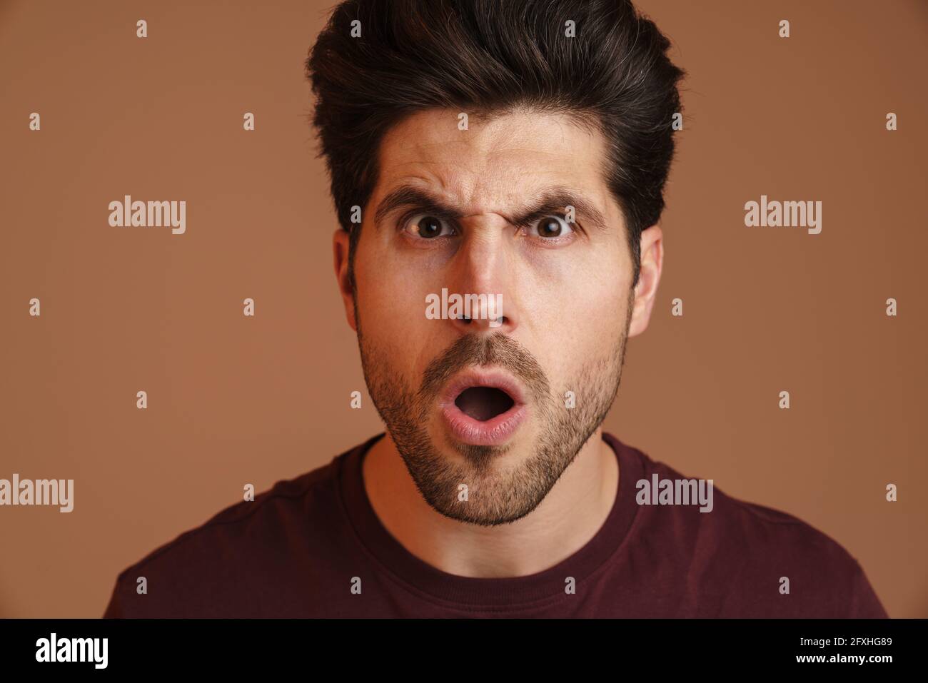 Dispiaciuto giovane non rasato esprimendo sorpresa sulla macchina fotografica isolata sopra sfondo beige Foto Stock