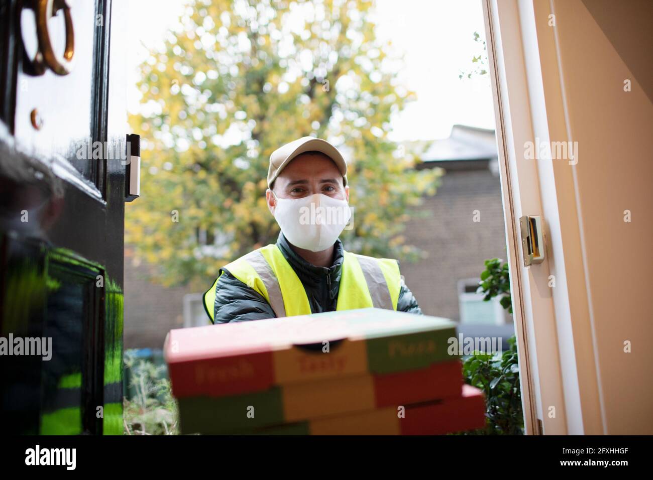 Consegna ritratto uomo in maschera viso consegna pizza alla porta d'ingresso Foto Stock