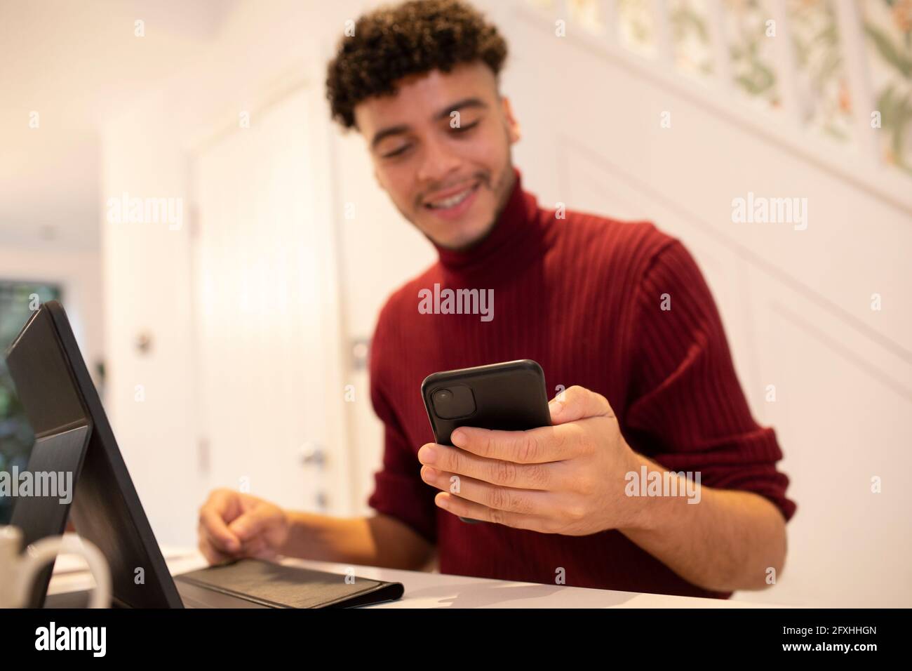 Giovane uomo con smartphone che lavora da casa al computer portatile Foto Stock