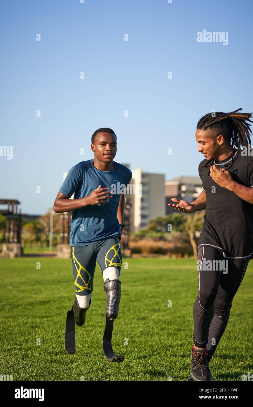 Allenatore tempo atleta amputato maschile che corre in erba soleggiato Foto Stock