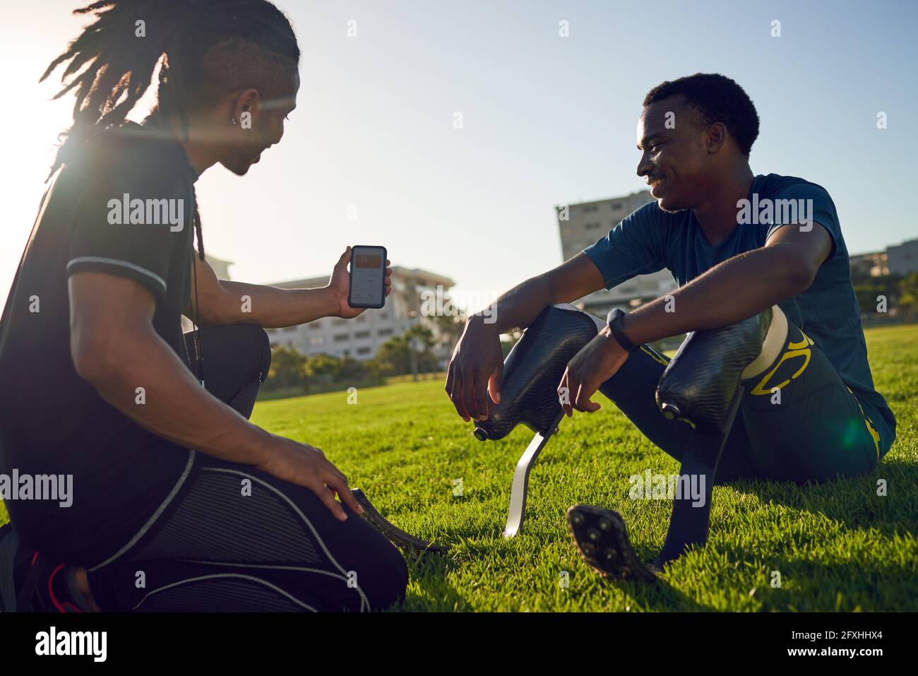 Allenati con uno smartphone che parla con l'atleta amputato in erba soleggiato Foto Stock