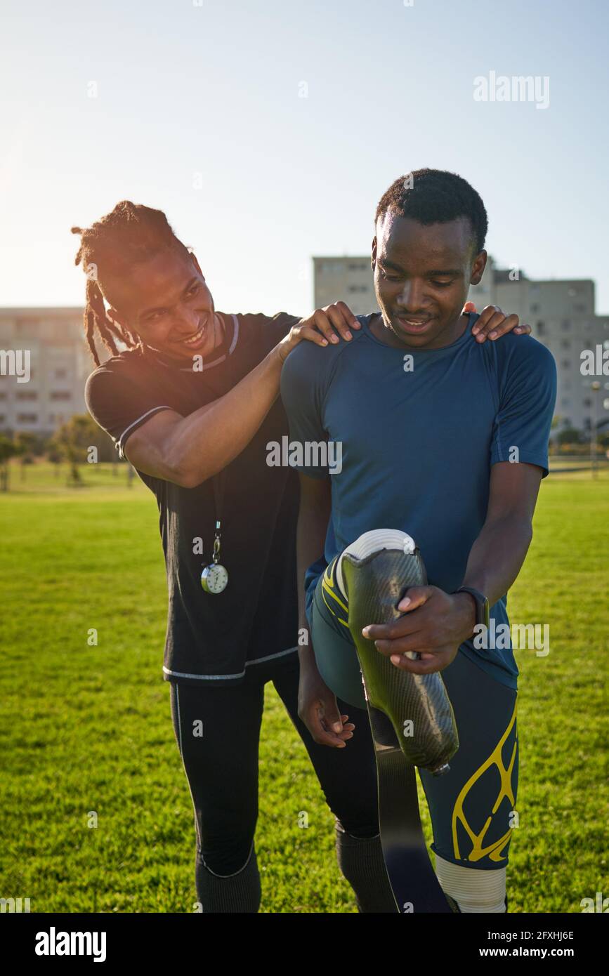 Allenatore che sostiene un giovane atleta maschile amputato che si estende nel parco Foto Stock