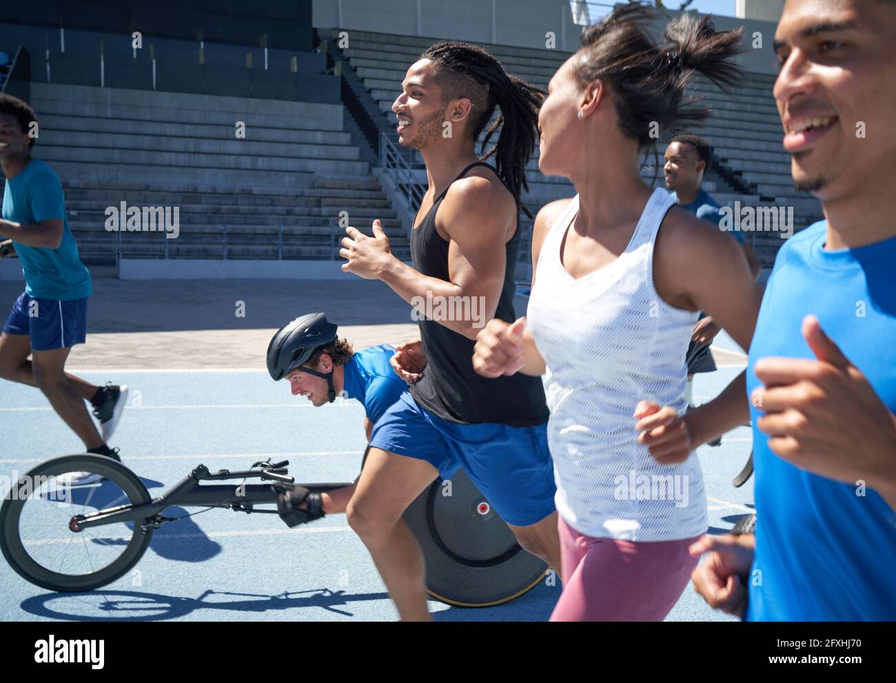 Atleti che corrono e in carrozzina sportiva su pista sportiva soleggiata Foto Stock