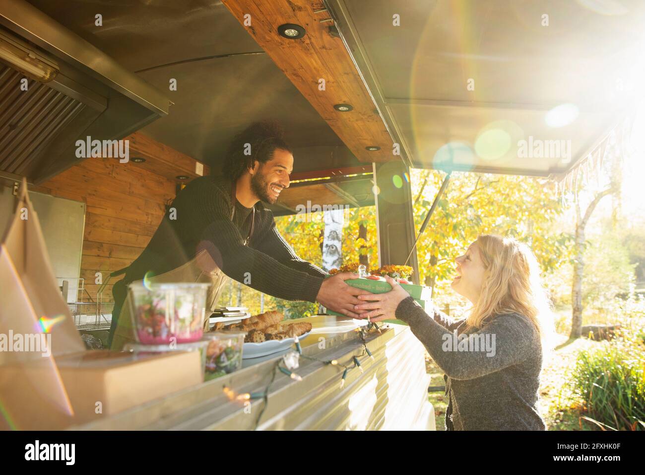 Buon proprietario del camion del cibo che serve il cibo al cliente in un parco soleggiato Foto Stock