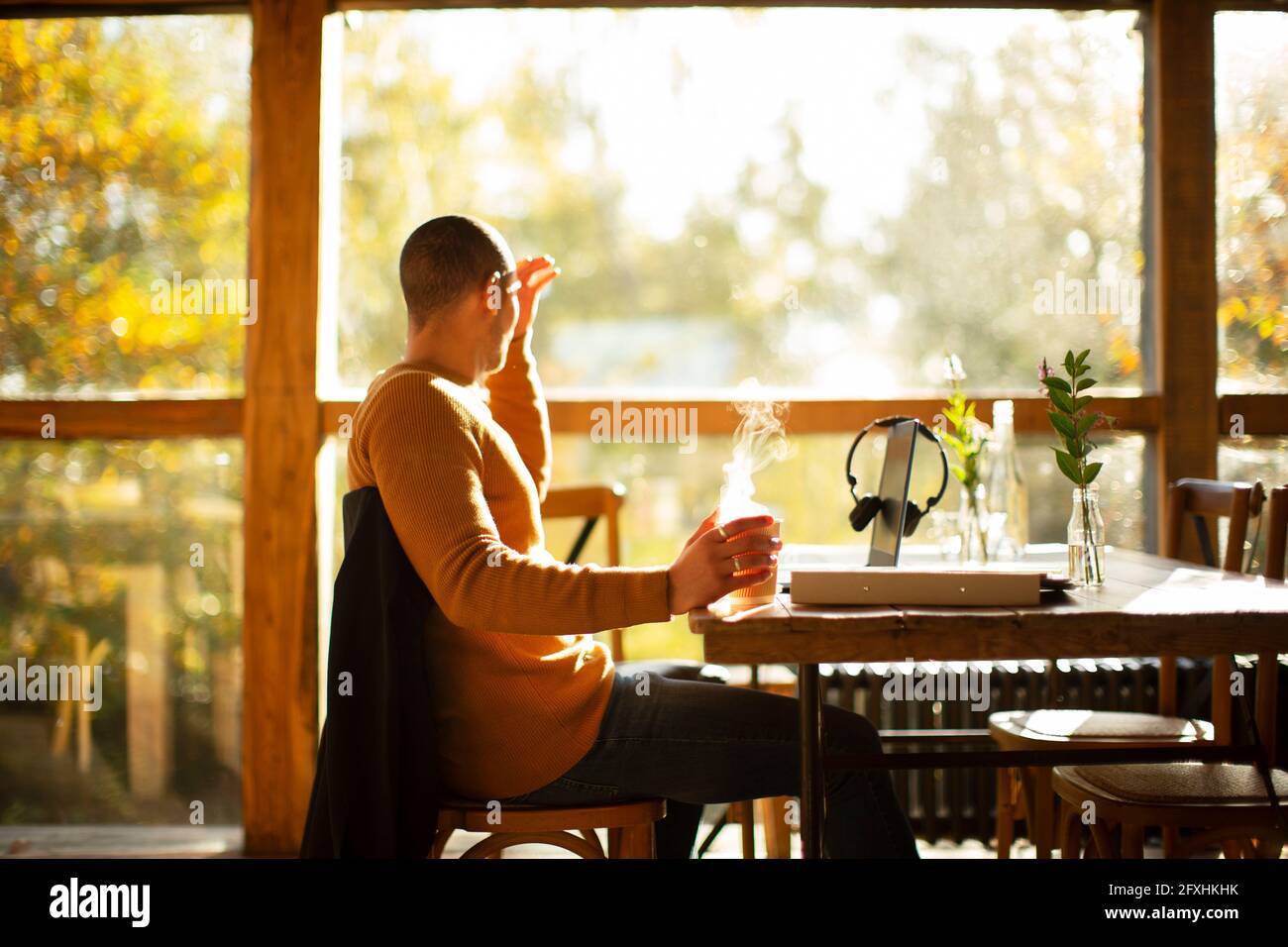 Uomo d'affari con caffe' caldo che lavora al tavolo in un soleggiato cafe' d'autunno Foto Stock