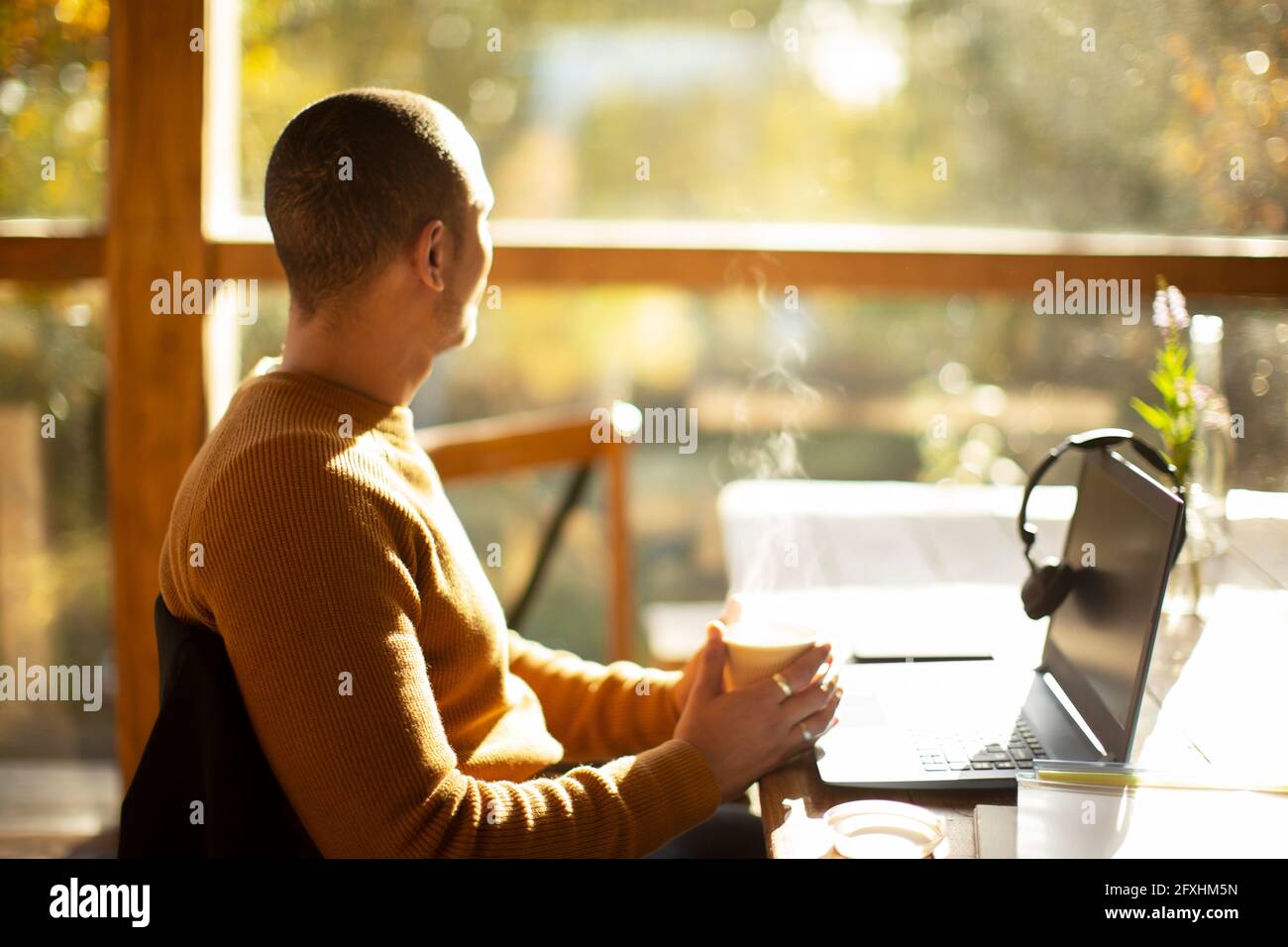 Uomo d'affari premuroso con caffè e computer portatile che si affaccia sulla finestra soleggiata Foto Stock